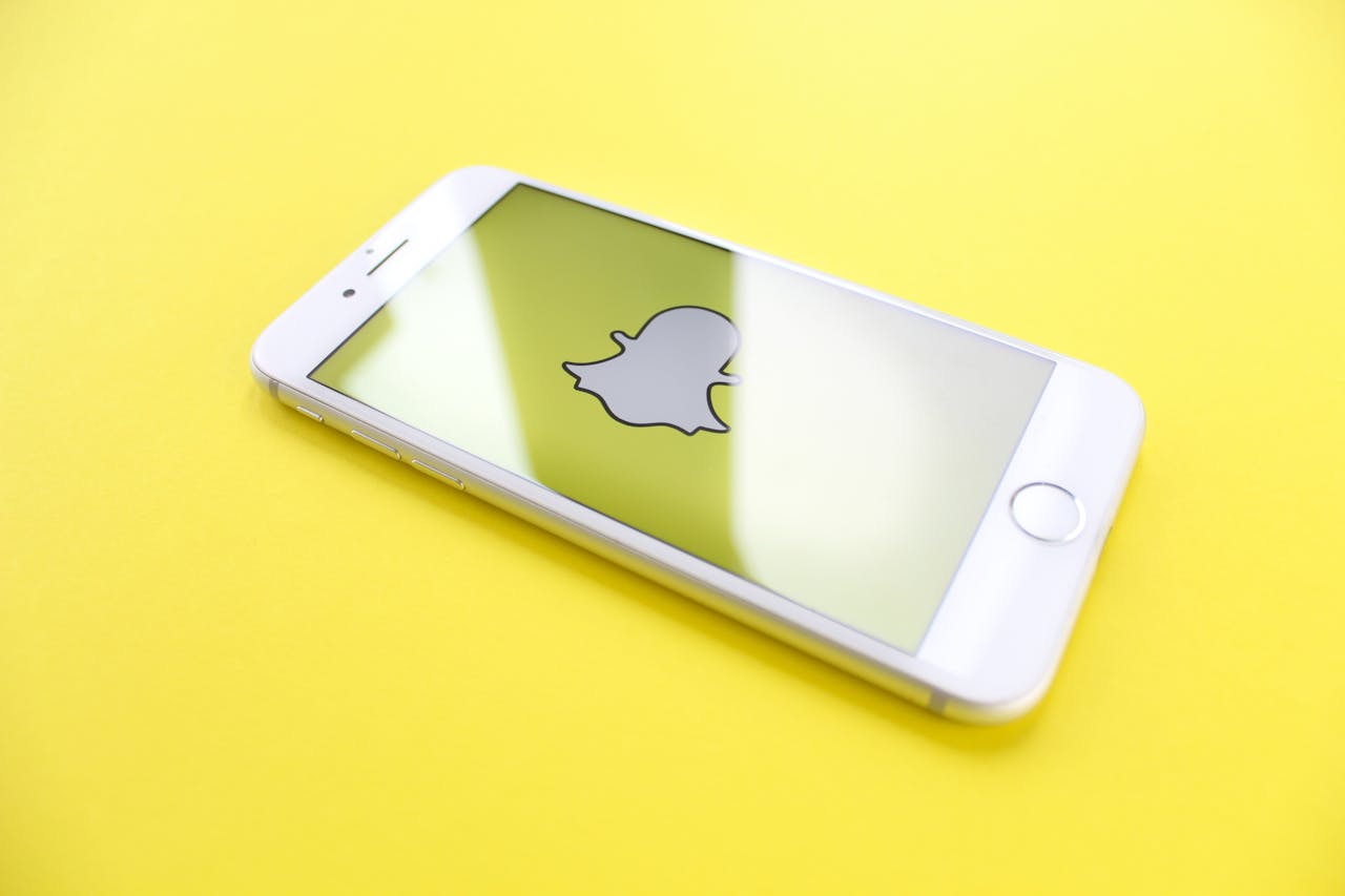 project-02-c White smartphone displaying Snapchat logo on a bright yellow background, angled view.