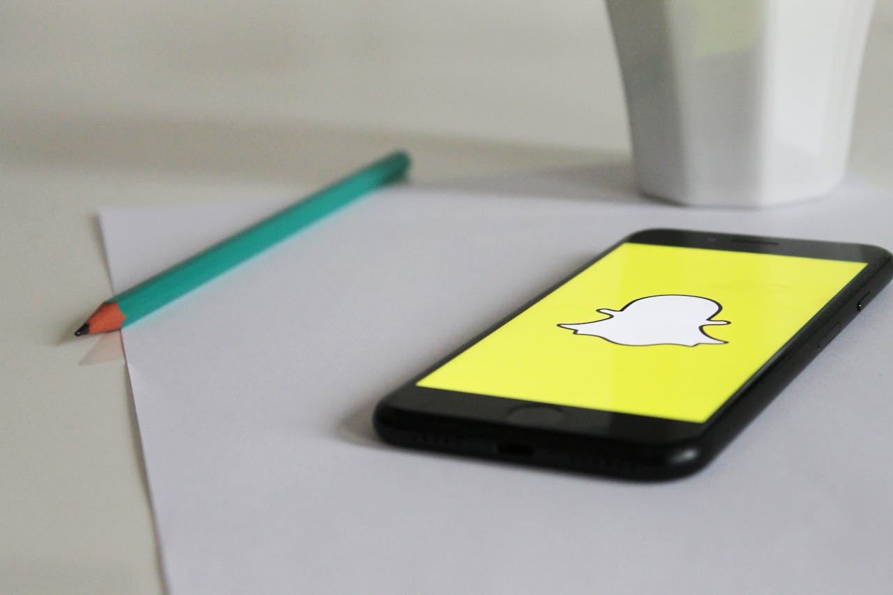 project-01-a Smartphone with Snapchat logo on a desk with pencil and mug, emphasizing social media and technology.