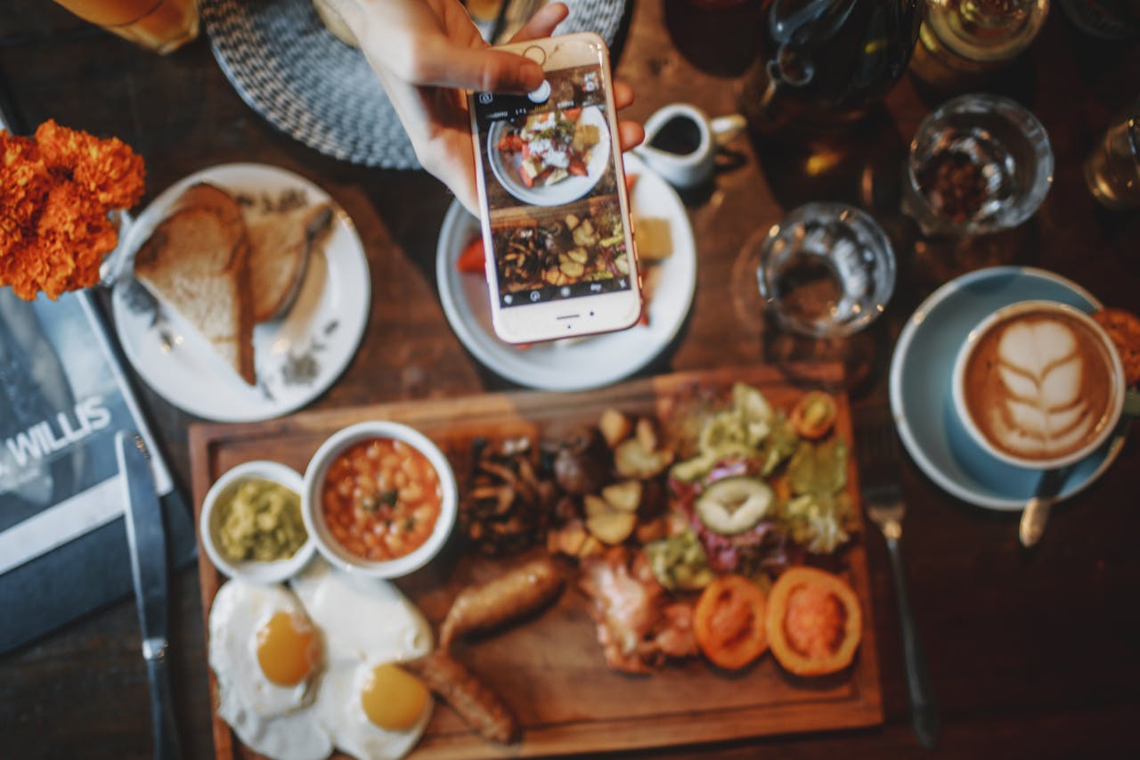 A hand capturing a vibrant brunch spread with a smartphone in a cozy cafe setting.