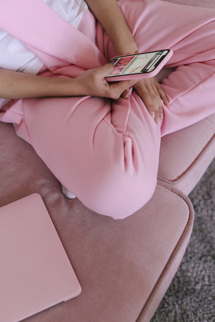 about-header Close-up of a woman using a smartphone on a pink couch with a laptop nearby, creating a cozy and modern tech-savvy vibe.